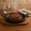 REGENT COOKWARE CAST IRON OVAL PAN WITH 2 HANDLES ON A WOODEN BOARD, (225X120X55MM)